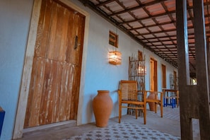 A corridor with wooden doors, a large terracotta pot, and a wooden chair. - Ecocharme Pousada Netuno (Fernando de Noronha)