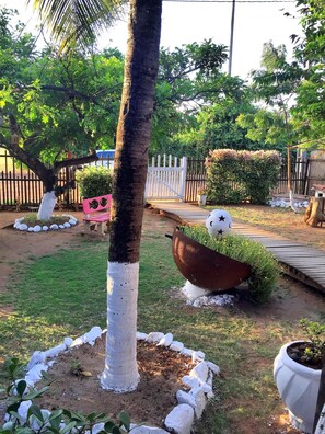 A garden with a palm tree, a wooden bench, a large planter, and a white fence.
