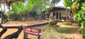 A rustic outdoor area with a wooden deck, a red bench, and a large planter.