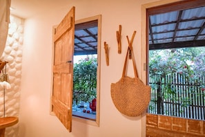 A room with a wooden door, a woven bag, and a window with a view of greenery. - Ecocharme Pousada Netuno (Fernando de Noronha)