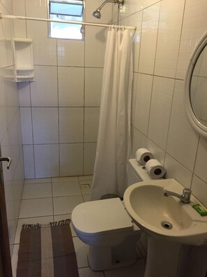 Ett litet badrum med toalett, handfat och dusch. Det ligger två toalettpappersrullar på handfatet.
