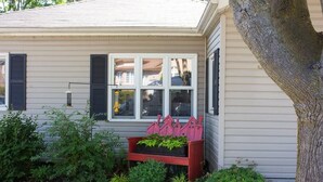 A house with a red bench in front, a window with shutters, and a tree to the right. - The Cobourg Creek Cottage (Cobourg)
