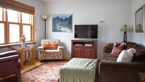 A living room with a sofa, armchair, TV, and a painting on the wall. - The Cobourg Creek Cottage (Cobourg)