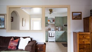 A cozy living room with a brown sofa, a wooden side table, and a green throw blanket. A wooden cabinet and a framed picture are on the right. - The Cobourg Creek Cottage (Cobourg)