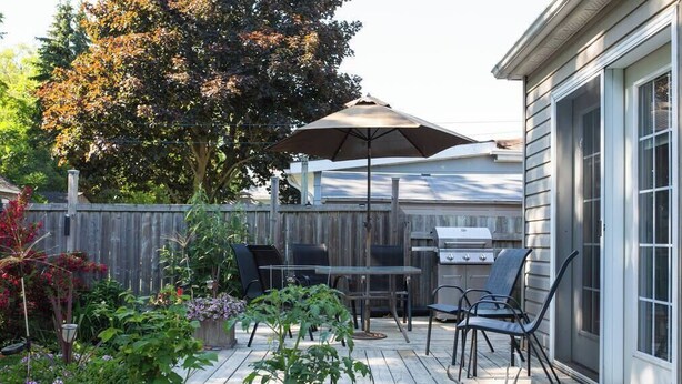 A wooden deck with a grill, chairs, and a table. - The Cobourg Creek Cottage (Cobourg)