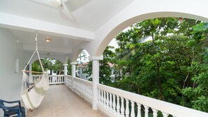 A covered outdoor area with a white balustrade, a hammock, and a view of lush greenery.