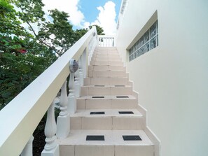 Una escalera con barandillas blancas y peldaños color beige que lleva a un balcón.