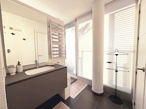 A modern bathroom with a large mirror, two sinks, a towel rack, and a floor lamp.