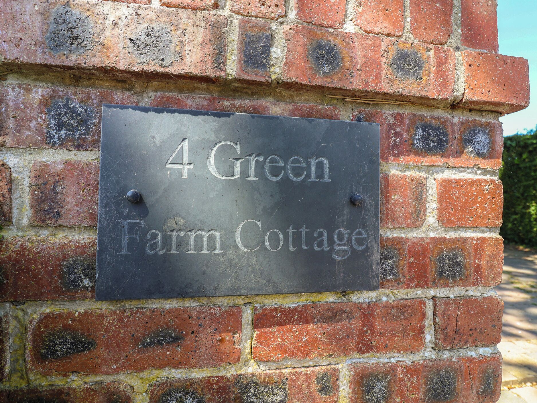 Una señal en una pared de ladrillo que dice '4 Green Farm Cottage'.