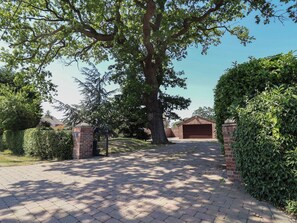 A paved driveway leading to a garage, surrounded by lush greenery and a large tree. - 4 Green Farm Cottage (Chester)