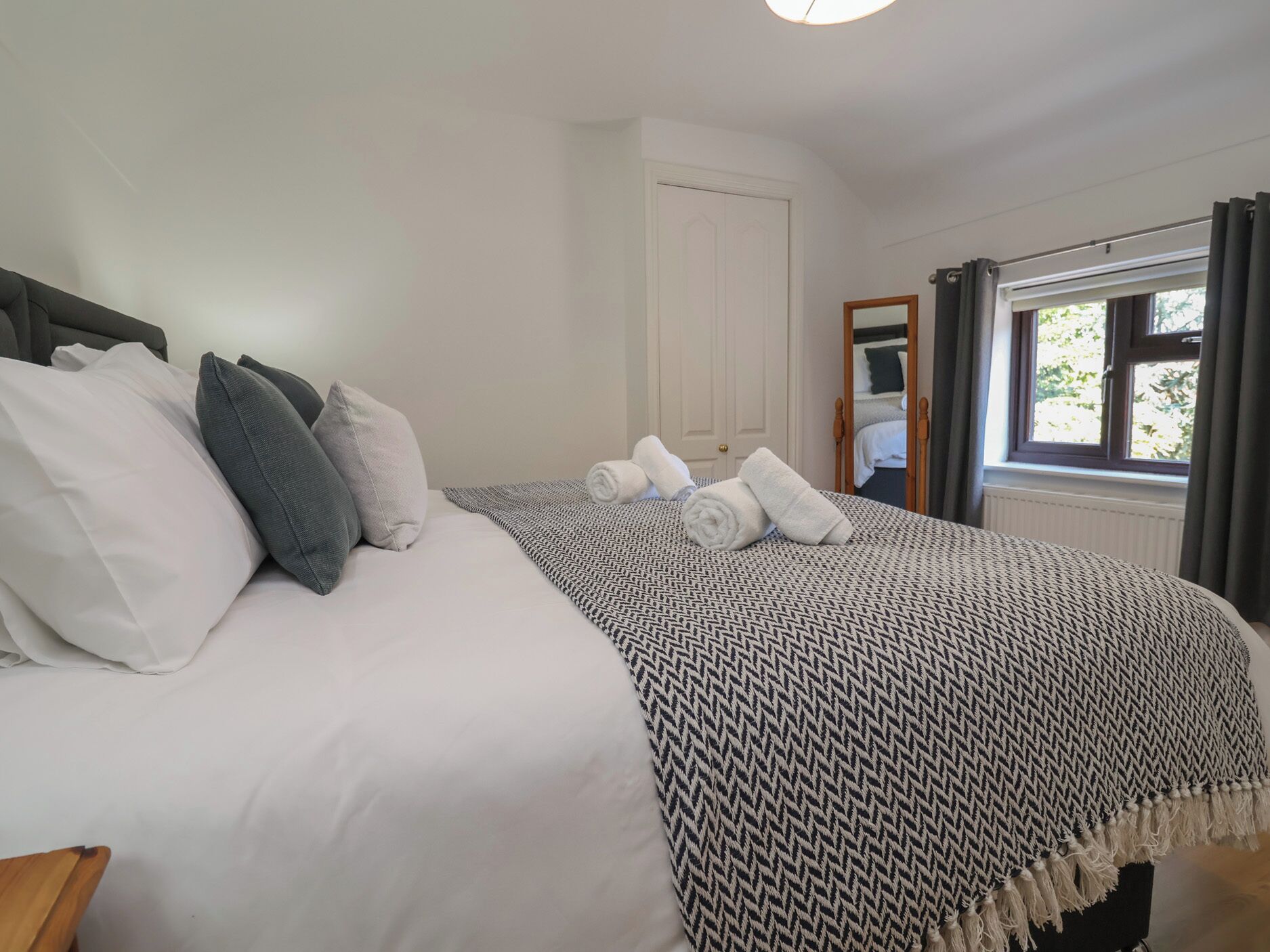 A neatly made bed with white and grey bedding, a patterned throw blanket, and rolled towels.