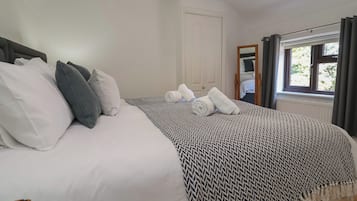 A neatly made bed with white and grey bedding, a patterned throw blanket, and rolled towels.