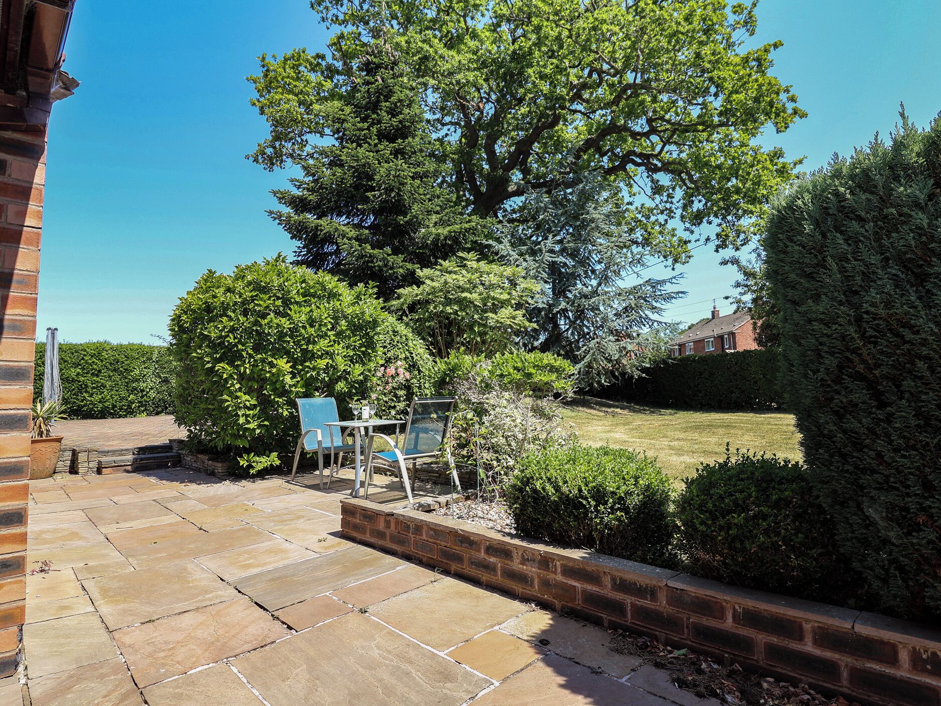 Un patio con piso de piedra, pared de ladrillo y un gran árbol que da sombra.