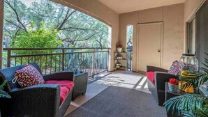 A balcony with wicker furniture, a ceiling fan, and a view of trees.