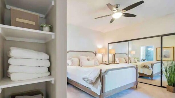 A bedroom with a bed, bedside lamps, a ceiling fan, a wardrobe, and a mirror.