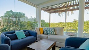 Una sala de estar moderna con un conjunto de sofá, una mesa de centro y vistas al verdor a través de amplios ventanales.