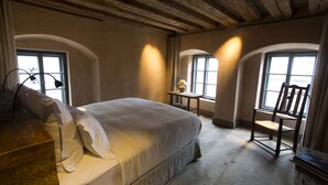 Un dormitorio con cama, una silla, una mesa y dos ventanas.