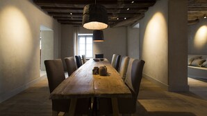 Una larga mesa de comedor de madera con sillas, un lámpara colgante y una vista de una ventana y un sofá al fondo.