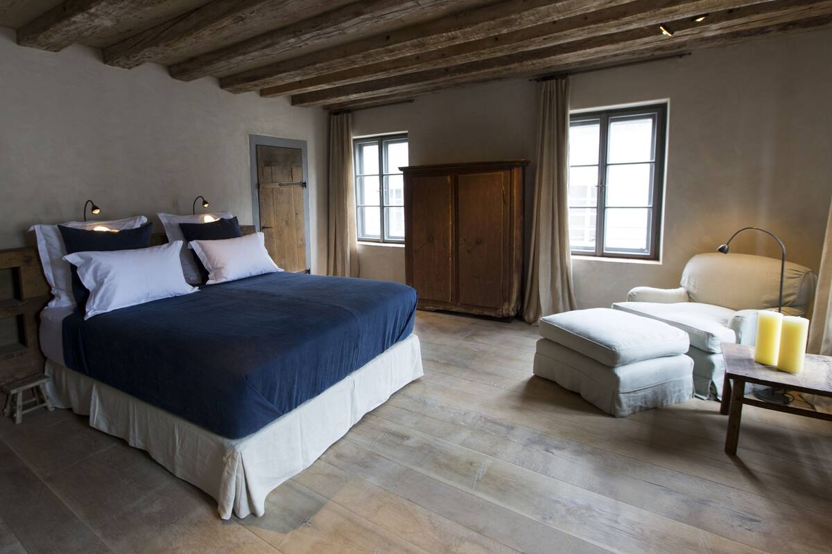 Un dormitorio con una cama grande, lámparas de noche, un armario, una silla y una mesa con velas.