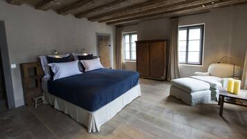 A bedroom with a large bed, bedside lamps, a wardrobe, a chair, and a table with candles.