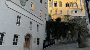 Una calle empedrada con edificios históricos, una destacada torre del reloj y un castillo al fondo.