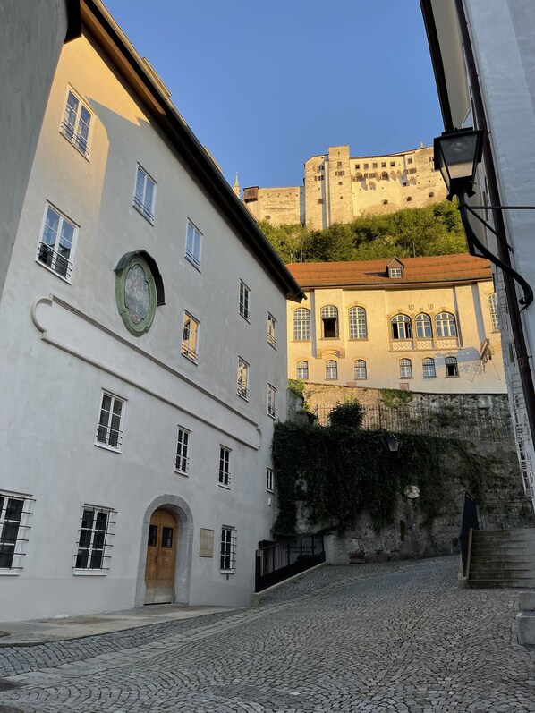Una calle empedrada con edificios históricos, una destacada torre del reloj y un castillo al fondo.