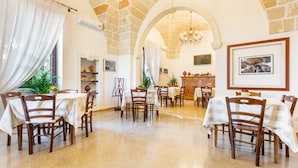 A dining area with tables and chairs, stone arches, and a chandelier. - Tenuta Cavalieri - Camera Quadrupla (Leverano)