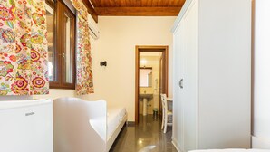 A hotel room with a bed, a small white desk, a chair, and a window with curtains.