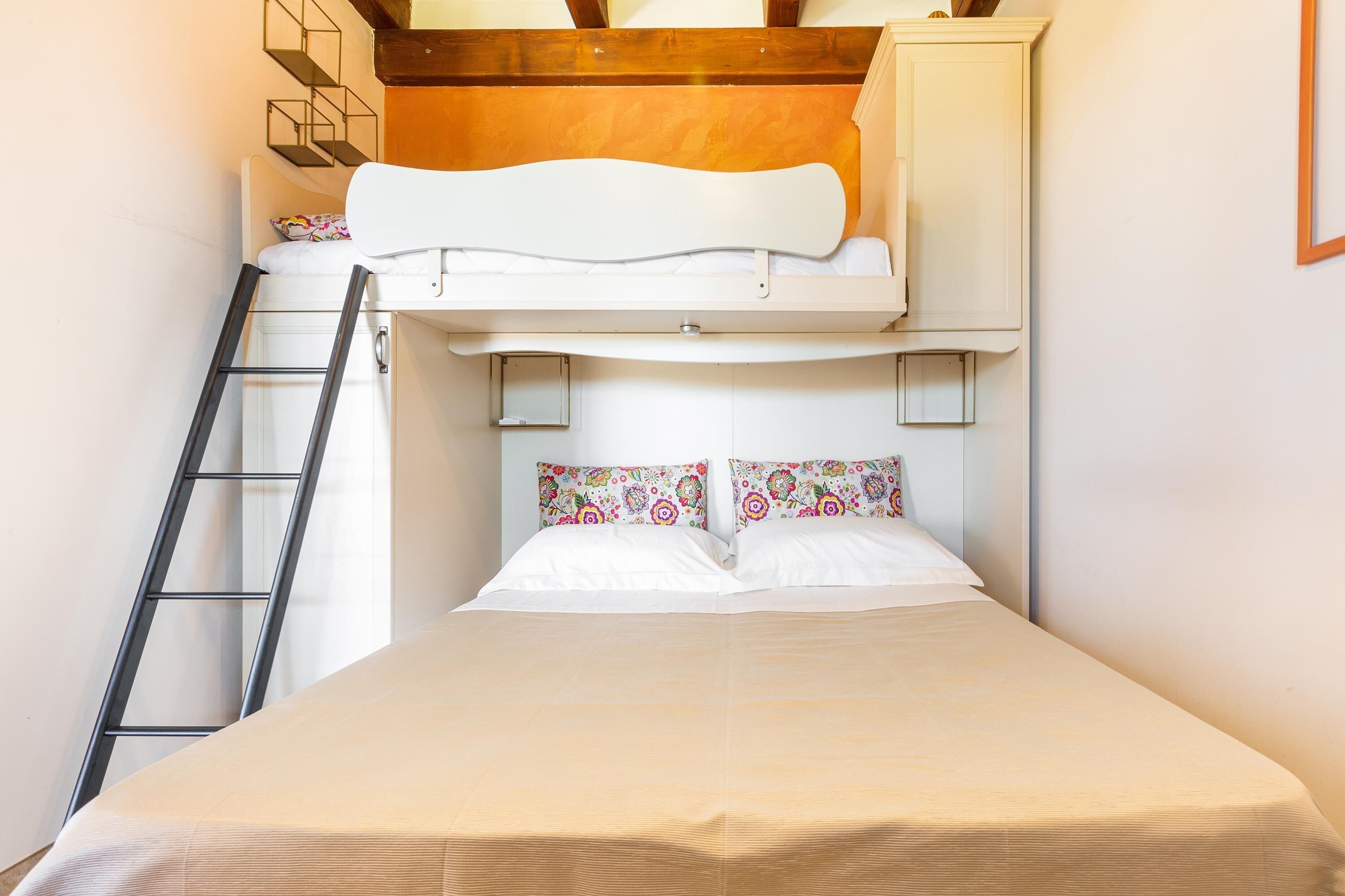 Een stapelbed met een ladder, een wit hoofdbord en gekleurde kussens.
