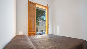 Ein Schlafzimmer mit einem Bett, einer Holztür und Blick ins Freie.