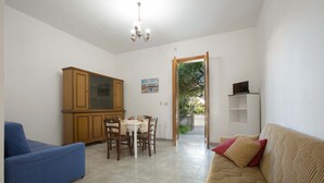 Ein Wohnzimmer mit einem blauen Sofa, einem beigen Sofa, einem Holzschrank, einem Esstisch mit Stühlen und einem Fernseher auf einem Lowboard.