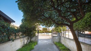 Ein Betonweg, der von niedrigen Mauern gesäumt wird und zu einem Tor mit Baumallee führt.