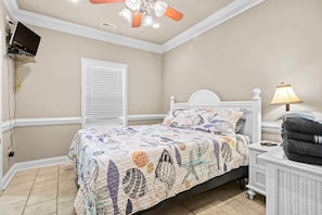 A bedroom with a bed, a bedside table, a lamp, a ceiling fan, and a TV mounted on the wall. - Upscale Beach House-Linens|Golf Cart|Quiet Area (Myrtle Beach)