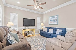 A living room with a ceiling fan, a flat-screen TV, a blue sofa, and a brown couch. - Upscale Beach House-Linens|Golf Cart|Quiet Area (Myrtle Beach)