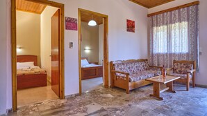 A room with a wooden ceiling, a stone floor, a bed, a sofa, two chairs, and a table with a glass. - Theodora Apartment 1 Agios Stefanos Corfu (Corfu)