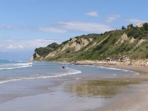 A beach with a sandy shore, a few umbrellas, and a hillside with vegetation.