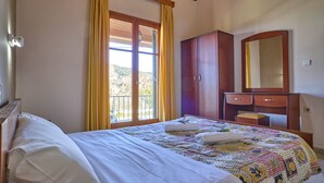 A bedroom with a bed, a wooden wardrobe, a mirror, and a window with curtains. - Theodora Apartment 1 Agios Stefanos Corfu (Corfu)