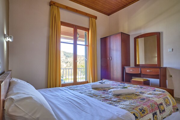 A bedroom with a bed, a wooden wardrobe, a mirror, and a window with curtains.