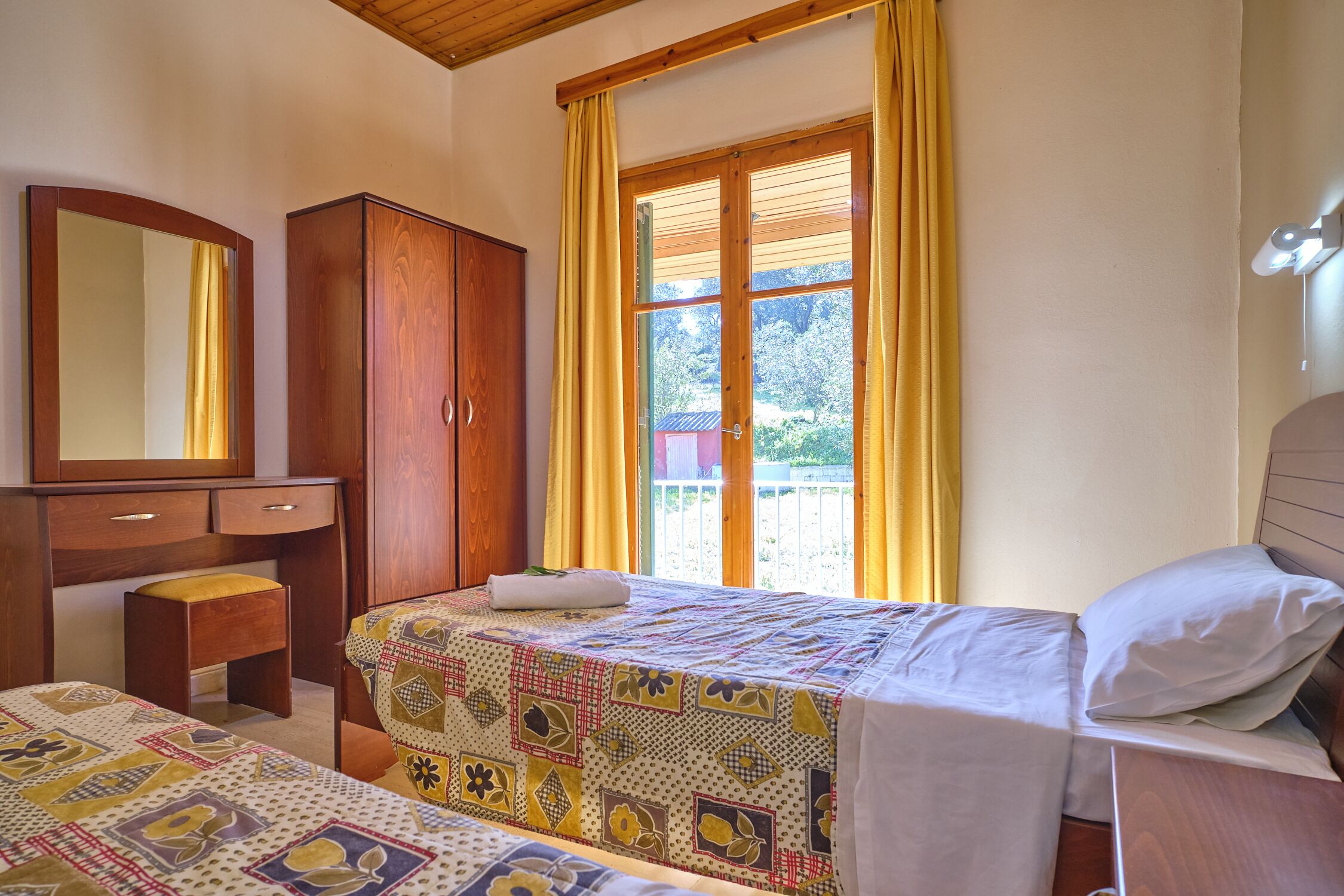 Une chambre à coucher avec un lit, une armoire en bois, un bureau et une fenêtre avec des rideaux.