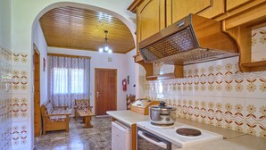 A compact kitchen with wooden cabinets, a stove, and a dining area with a table and chairs. - Theodora Apartment 1 Agios Stefanos Corfu (Corfu)