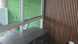 A modern office space with a large desk, two chairs, and a view of green artificial grass through large windows.