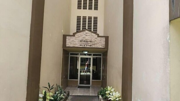 A narrow corridor with a central entrance, flanked by planters with greenery, leading to a building with a tiled roof and a decorative facade.