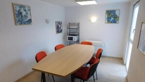 Une salle de conférence avec une table en bois et des chaises rouges, des murs blancs et des œuvres d’art.