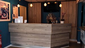 Un comptoir d’accueil avec un revêtement en bois, des luminaires suspendus, un téléviseur fixé au mur et un miroir décoratif en forme de soleil.