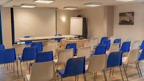 Une salle de conférence équipée d’un tableau blanc, d’un projecteur et d’une table entourée de chaises, le tout disposé pour une réunion.