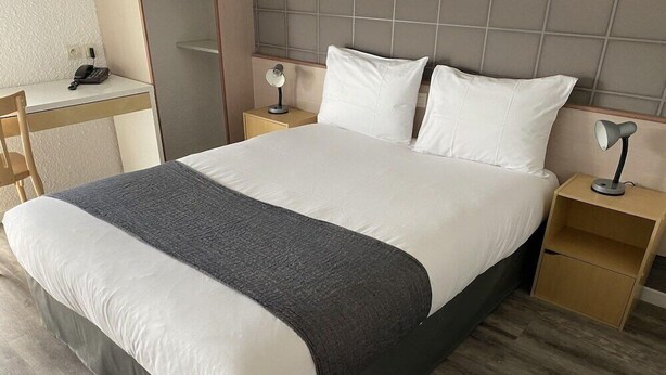 Une chambre d’hôtel moderne, dotée d’un grand lit, de tables de chevet, d’un bureau et d’un téléphone.