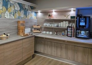 A modern kitchen with wooden cabinets, a coffee machine, and various kitchenware on the counter. - Brit Hotel Aries Argentan (Argentan)