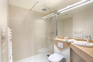 A modern bathroom with a glass-enclosed shower, a white toilet, a sink with a mirror, and a towel rack. - Brit Hotel Aries Argentan (Argentan)