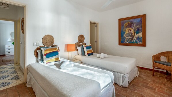 Une chambre d’hôtel avec deux lits, un tableau au mur et une chaise en osier.
