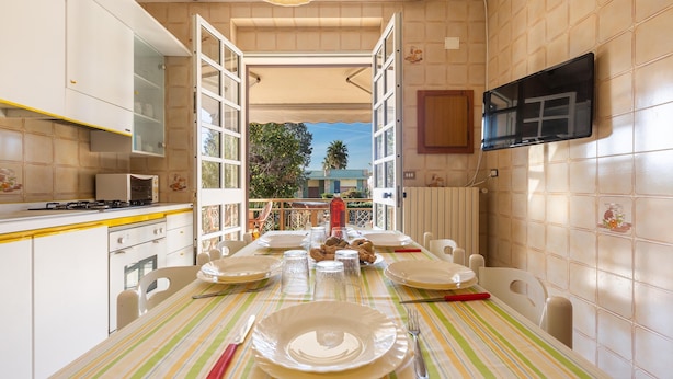 A dining area with a table set for four, a television mounted on the wall, and a view of the outdoors. - 3214 Villa Serenè - Appartamento A by Barbarhouse (Racale)